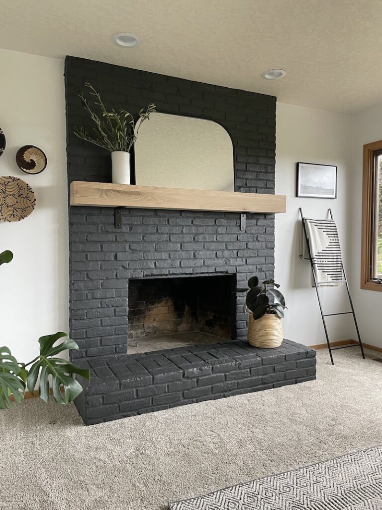 living room with black painted brick fireplace with oak wood mantel