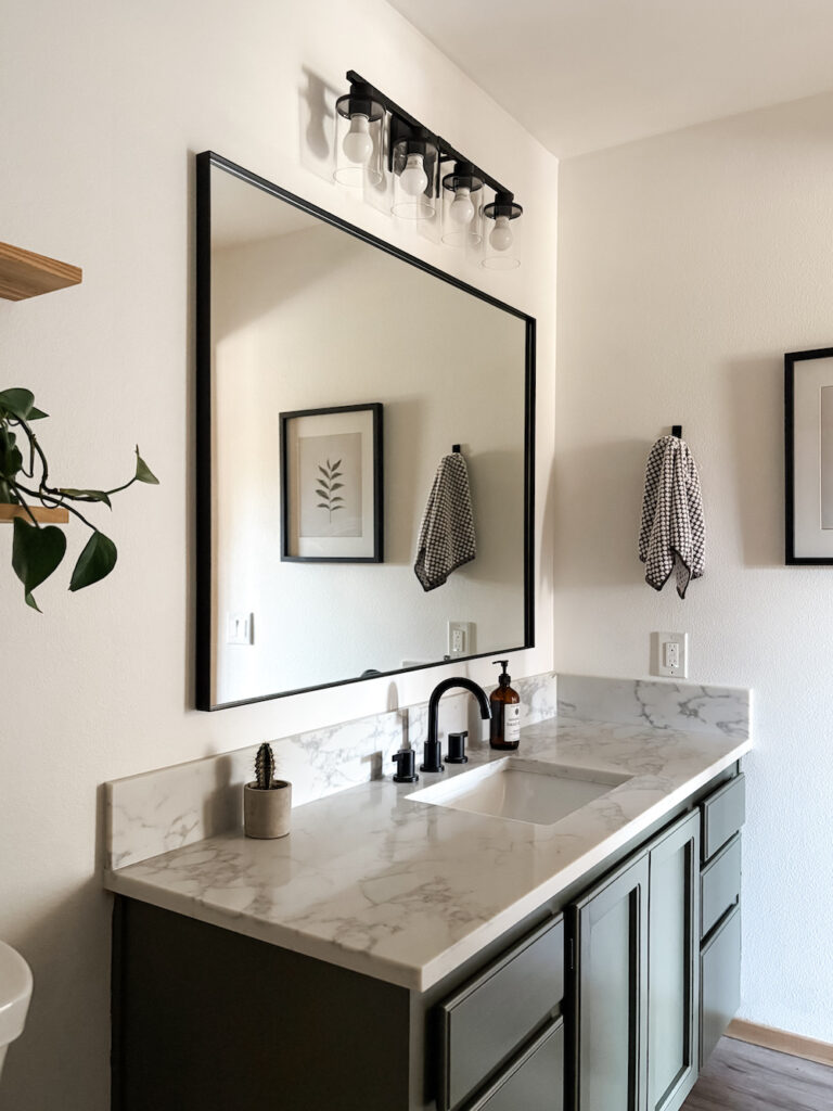 updated bathroom with forest green cabinets, quartz countertops, black hardware, metal mirror, and black and white decor