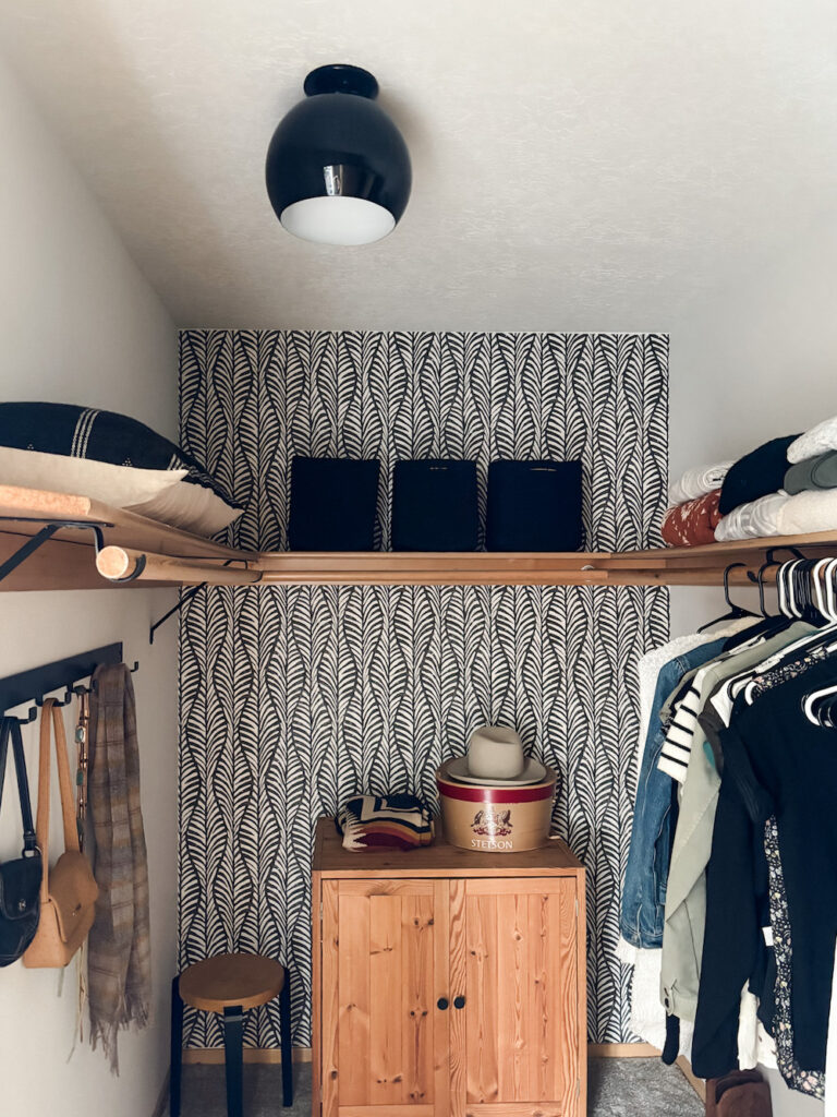 walk in closet with wall paper, black basket, light fixture, and hook rack