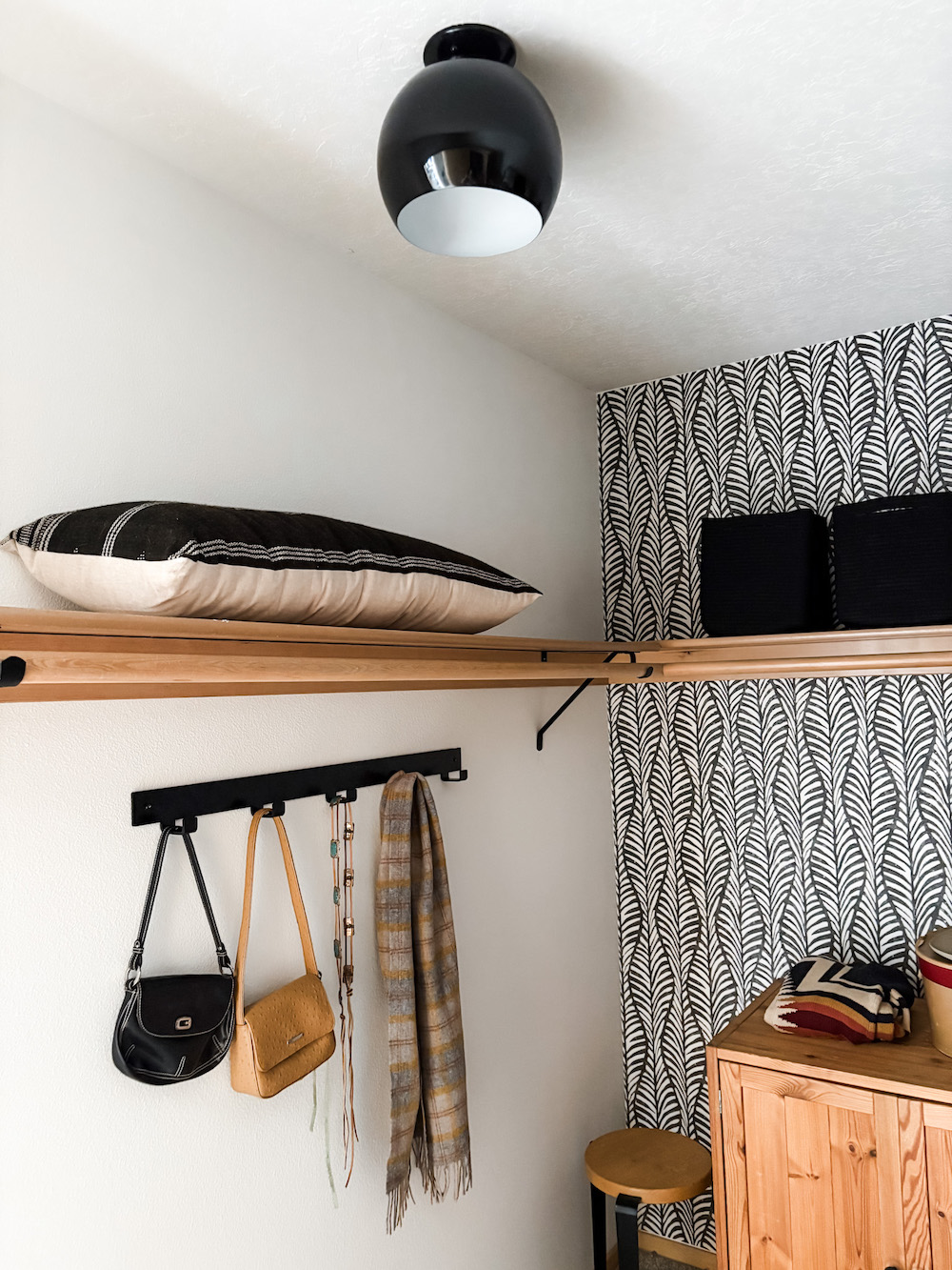 walk in bedroom closet with black and white peel and stick wall paper, globe light fixture, hook rack, wood shelves, and baskets