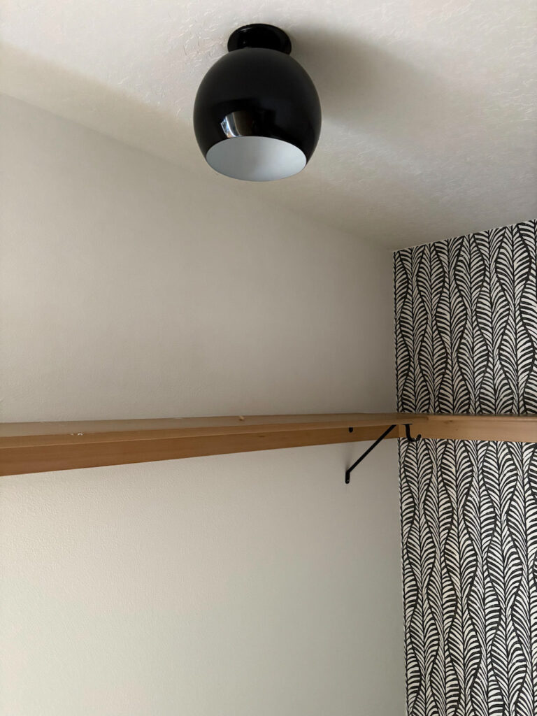 black globe light fixture in closet with white walls, wallpaper, and wood shelf