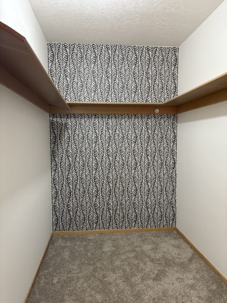walk in closet with painted white walls, black and white wallpaper, and wood shelves