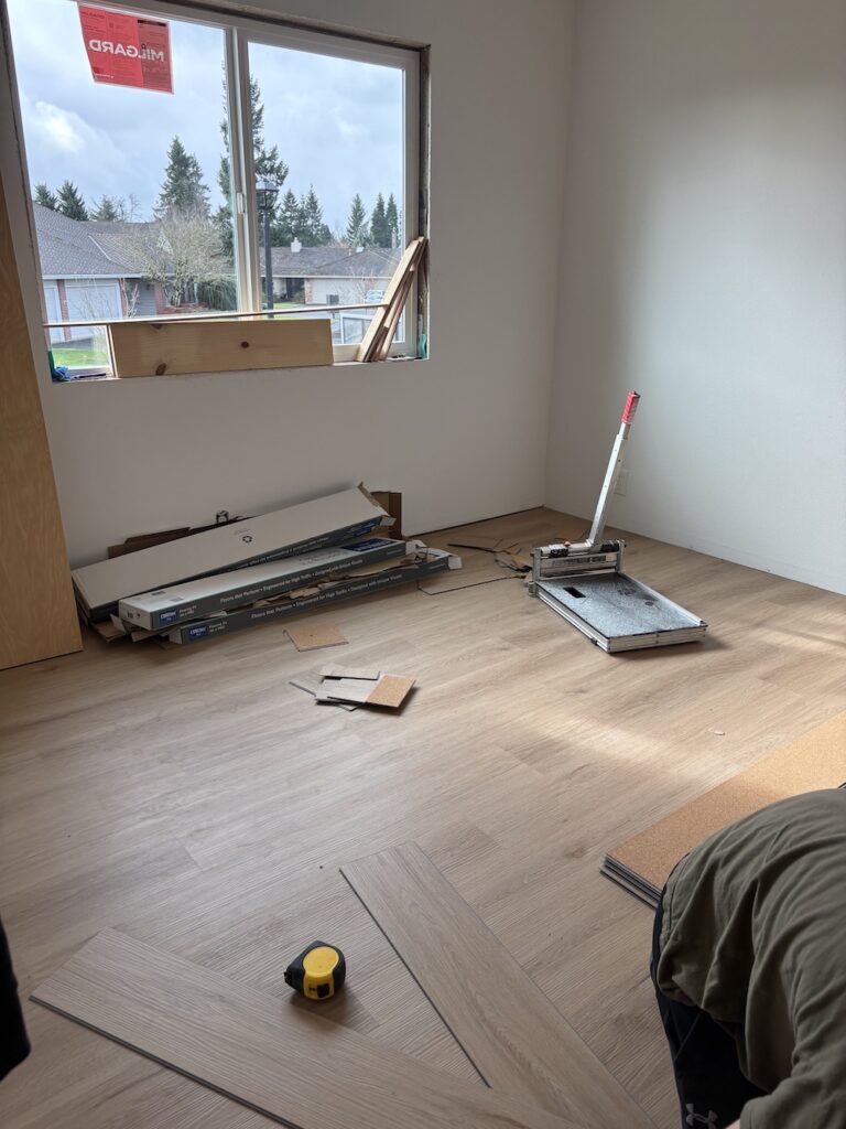 Bedroom with COREtec Springfield Oak LVP being installed. There are planks, tools, and the side of a man installing.