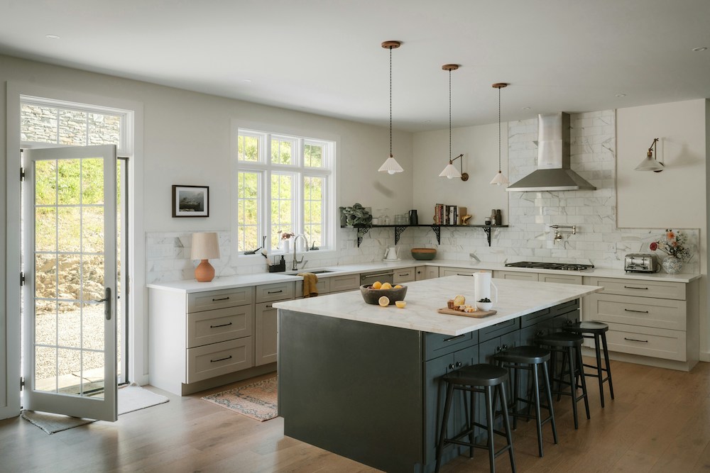 modern, neutral kitchen with light gray cabinets and dark kitchen island. There are hanging pendant lights, lamp, and bar stools with a wood floor.
