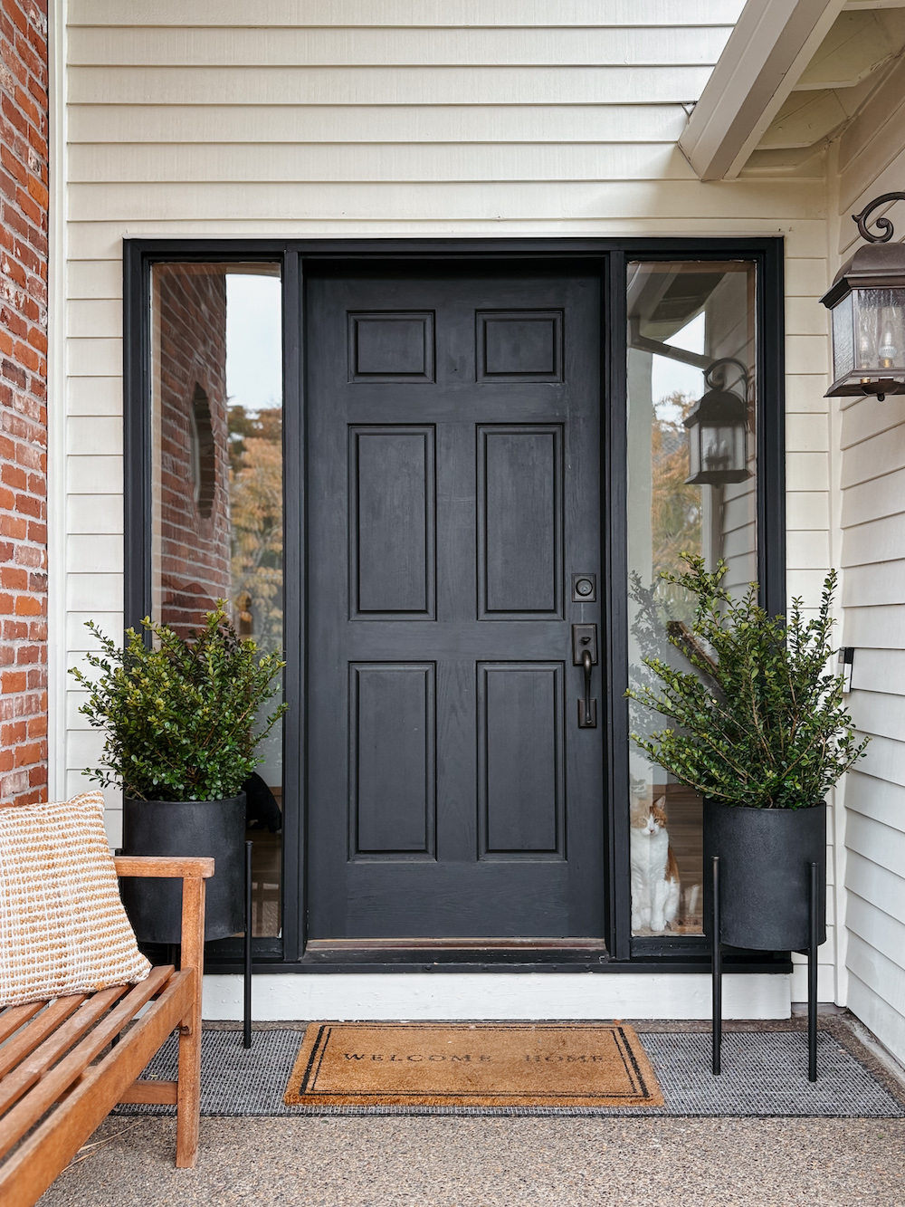 cream house with black front door, welcome mat, bench, and plants