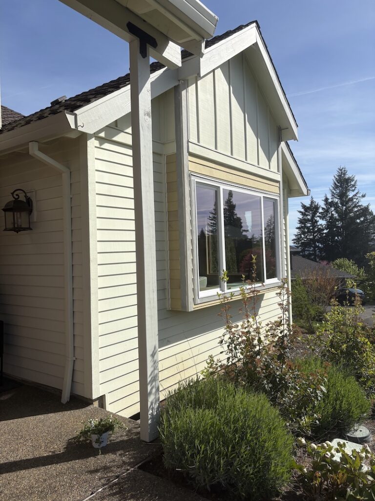 creamy yellow house with a column and large window and shrubs out front