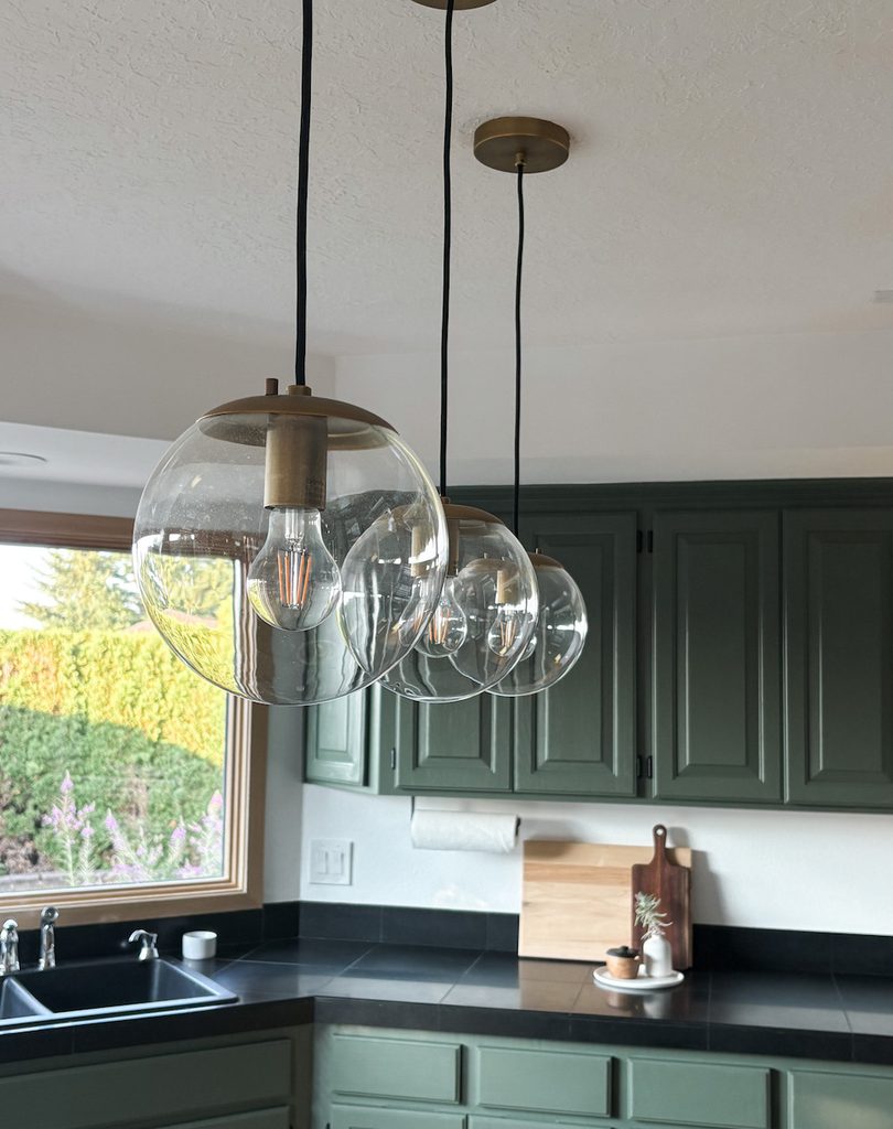 hanging pendant lights with brass hardware in kitchen with green painted cabinets in background