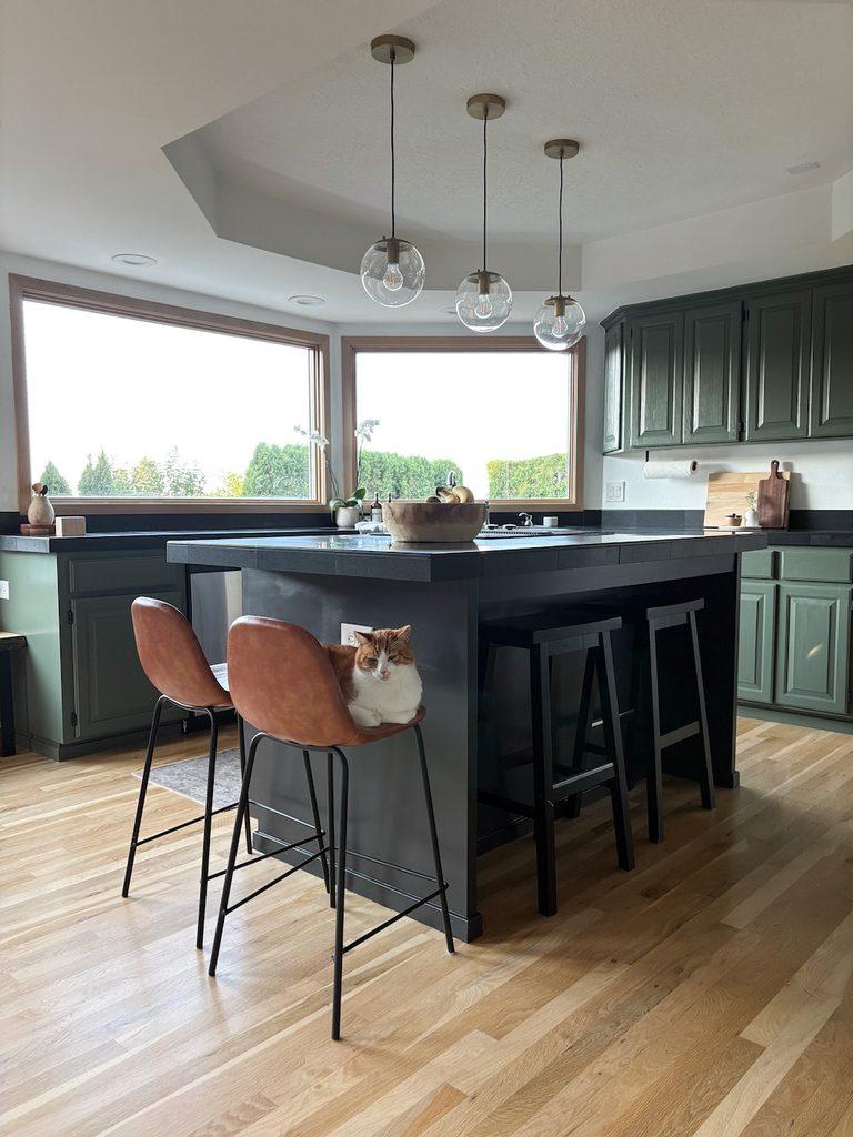 cat sitting on bar stool in kitchen with green painted cabinets and soft black painted kitchen island